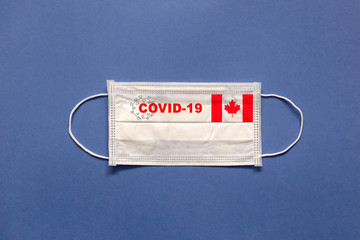 Flag of Canada and inscription COVID-19 on a medical mask on a blue background. Healthcare and medical concept. Pandemic virus COVID-19