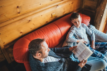 Father reading book to son in cozy country house on a Global Coronavirus COVID-19 pandemic Outbreak days. World 2019–20 coronavirus pandemic, home education and Stay at Home concept image.