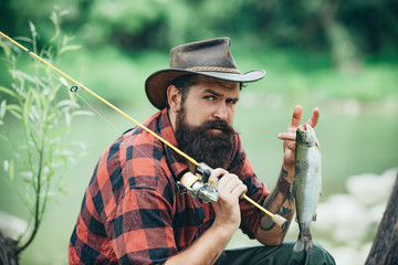 Portrait of man on holiday. Fishing background. Fly fishing adventures. Man dressed in shirt fishing with rod on the lake. Weekend time. Man fisherman catches a fish.