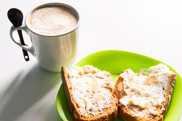 Cup of coffee with milk with a spoon and a green plate with cottage cheese toast