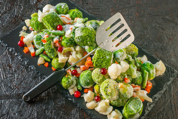 Set of frozen vegetables and fruits on a black kitchen board.