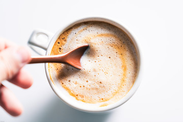 Hand stirring a cup of creamy coffee with a ceramic spoon