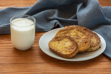 French toast - Przenice - slices of bread soaked in beaten eggs and milk and fried, with a glas of yogurt on a wooden table. Eggy bread, Bombay toast, German toast, gypsy toast or poor knights