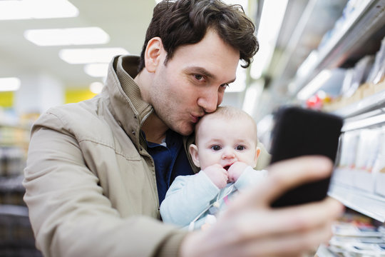 Affectionate father and baby daughter taking selfie in supermarket
