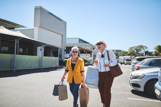 Happy senior women with shopping bags in sunny parking lot