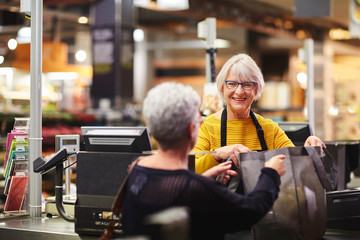 Friendly senior female cashier helping customer supermarket checkout