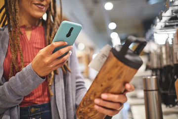 Woman with smart phone photographing insulated bottle in store