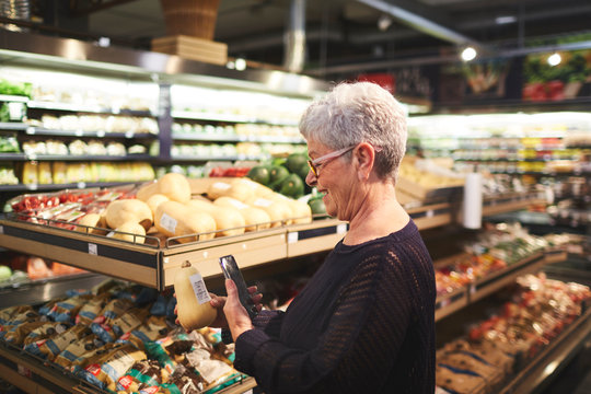 Senior woman with smart phone shopping in supermarket produce section