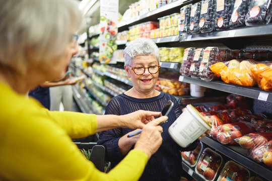 Senior women with smart phone grocery shopping in supermarket
