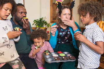 Multiethnic family eating decorated Halloween cupcakes
