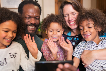 Happy multiethnic family waving and video chatting with smart phone