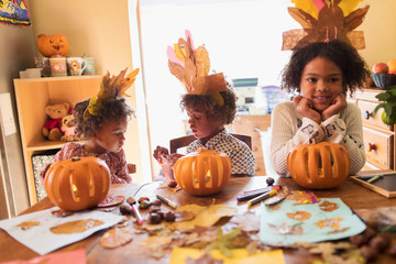Brother and sisters with turkey hats carving pumpkins at table