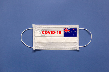 Flag of New Zealand and inscription COVID-19 on a medical mask on a blue background. Healthcare and medical concept. Pandemic virus COVID-19