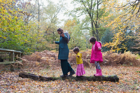 Mother and daughters balancing on fallen log in autumn woods