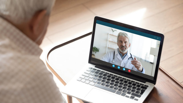 Back view of mature man have video call consultation with male doctor using laptop Webcam, close up of elderly male patient talk speak with GP or physician at home, discuss illness, consult online