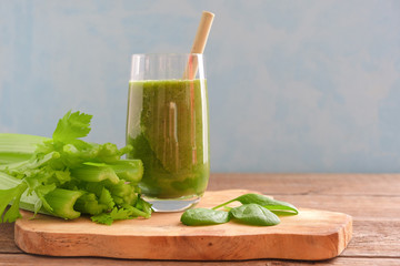 A glass with a green smoothie and a bamboo cocktail straw is standing on a wooden board. Nearby are bunches of celery and spinach and parsley leaves. Useful snack. Vegan, vegetarian drink. Copy space