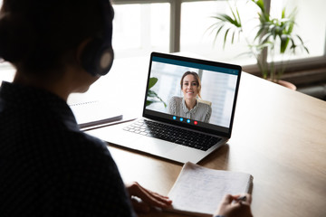 Back view of female employee sit at desk at home have Webcam conference on laptop with business...