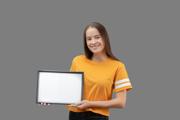 Young girl holding a horizontal blue frame with white mockup in her hands, smiling, isolated on a...