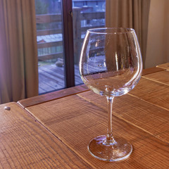 Empty wineglass on the wooden table on the window background.