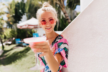 Charming caucasian female model with tanned skin raising glass of cocktail. Smilng joyful lady drinking favorite beverage with pleasure.