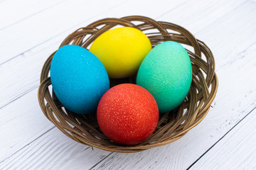 Four Easter colored plain eggs. A set of homemade eggs for Happy Easter holiday on a white wooden background. Boiled bright cooked eggs in a wicker basket