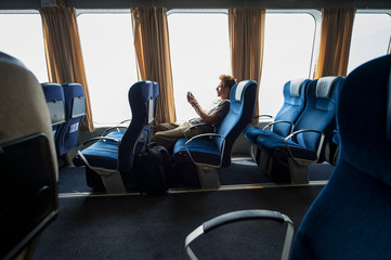 Lone traveler sitting in a row of empty blue window seats using his mobile phone - Powered by Adobe