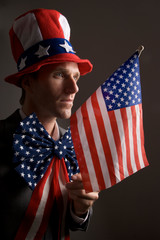 Portrait of patriotic American man wearing stars and stripes hat, and bow holding a flag in profile...