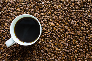White Cup with black espresso on scattered coffee beans close up top view with copy space