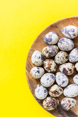 Natural organic fresh quail eggs on a wooden plate, yellow paper background. Copy space for text. 