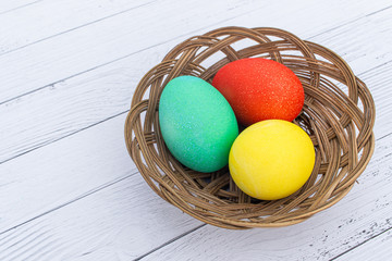 Three Easter colored plain eggs. Set of homemade eggs for Happy Easter holiday on a white wooden background. Boiled bright cooked eggs in a wicker basket