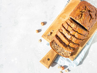 Homemade banana bread or cake with hazelnut on wooden cutting board, light stone background. Trendy...