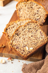 Homemade banana bread or cake with hazelnut on wooden cutting board, light stone background. Trendy soft shadows, atmospheric lighting, selective focus. Flat lay composition.
