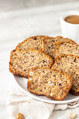 Sliced banana hazelnut bread on a ceramic plate with a cup of coffee. Morning atmospheric lighting, trendy soft shadows, selective focus. Idea for healthy diet breakfast.