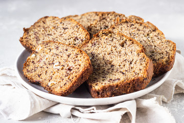 Sliced hazelnuts and banana loaf cake on a ceramic plate. Selective focus, top view.