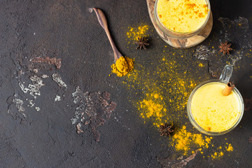 Golden milk or latte with turmeric (curcuma) powder with spices, dark brown concrete background. Trendy detox, immune boosting, anti-inflammatory healthy cozy drink. 