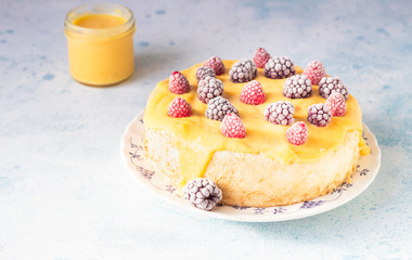 Angel food cake with lemon curd and frozen berries (raspberry and blackberry) on a plate, blue concrete background. Homemade chiffon cake.