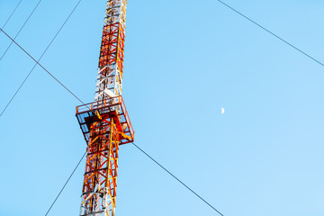 Funkmast mit Mond im Hintergrund, blauer Himmel