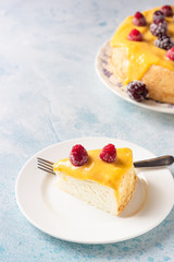 Slice of angel food cake with lemon curd and frozen berries (raspberry and blackberry), blue concrete background. 