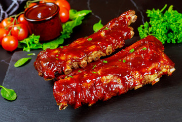 Baked juicy barbecue pork ribs with tomato, sauce and parsley.