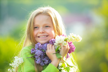 Fototapeta premium Young spring girl in spring garden. Young lady feeling happy in nature. Facial portrait of funny teenager girl. Girl with bouquet of lilac.