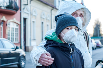 Fototapeta na wymiar A grandmother with her grandson are walking along the street in respiratory masks on their faces. Danger of infection with coronavirus covid-19. Quarantine Infection protection