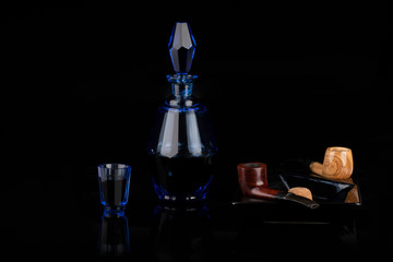 Obraz na płótnie Canvas Blue crystal carafe and smoking pipe on a black background.
