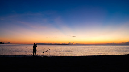 Fototapeta premium The silhouette of a photographer taking a photo of a beautiful sunset at tropical beach.
