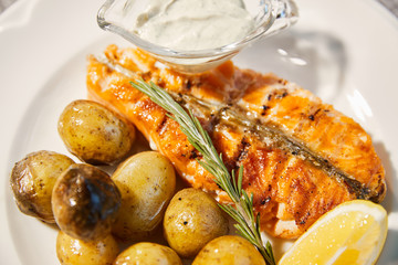 Grilled fish is on white plate with potatoes, lemon and sauce, Thyme branch, close up