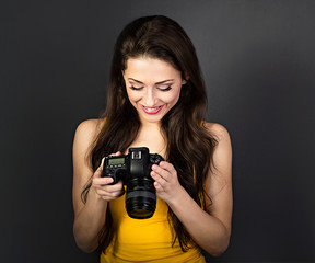 Happy toothy smiling young female photograph looking on the screen of camera and joying the photo on dark grey background