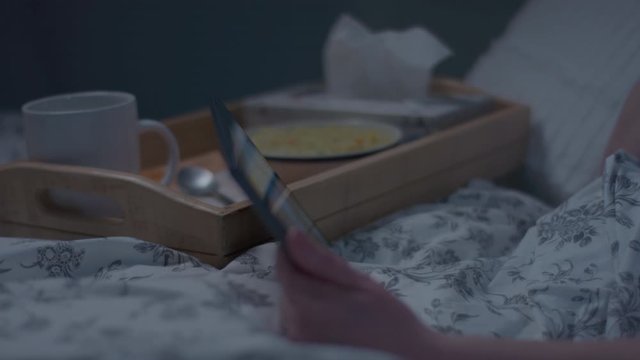 Woman Rests In Bed, Watches TV On Her Tablet, Grabs A Tissue To Blow Her Nose