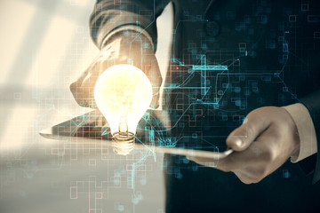 Double exposure of man's hands holding and using a digital device and bulb hologram drawing. Idea concept.