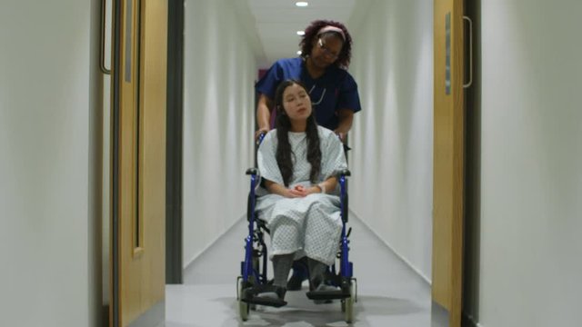 Nurse Pushes Patient In Wheelchair Down Corridor