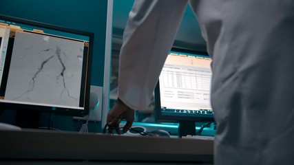 A dark-skinned African-American therapist watches the operation from a checkpoint. Monitors with X-rays and patient data in front of a professional surgeon. - Powered by Adobe