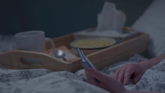 Sick Woman Watches Video On Smartphone At Night, She Takes A Spoonful Of Soup